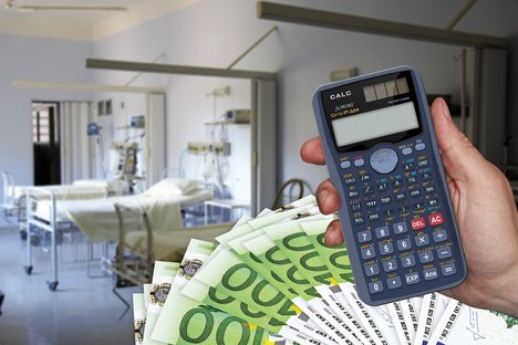 Das Foto zeigt im Hintergrund ein Krankenhauszimmer und im Vordergrund einen Taschenrechner und einige aufgefächerte Euro-Schein.