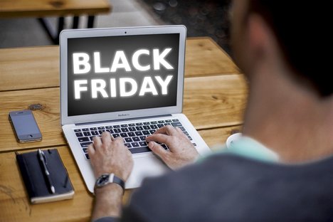 Das foto zeigt einen jungen Mann von hinten, der an einem Laptop sitzt. Auf dem Bildschirm des Laptops steht "Black Friday".