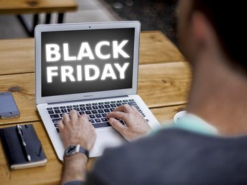 Das foto zeigt einen jungen Mann von hinten, der an einem Laptop sitzt. Auf dem Bildschirm des Laptops steht "Black Friday".