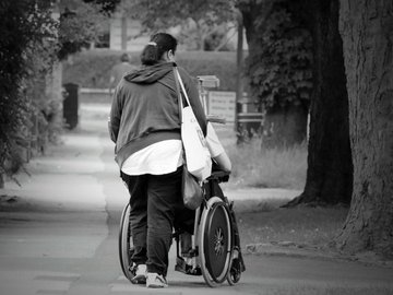 Das Foto zur Pressemitteilung der Linken NRW zum Equal Care Day zeigt eine Frau, die eine Person im Rollstuhl schiebt.