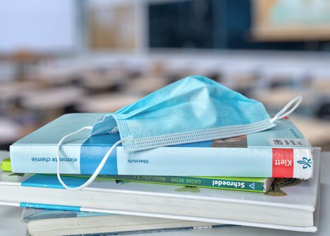 Das Foto zeigt einen Stapel Schulbücher, auf dem eine OP-Maske liegt.