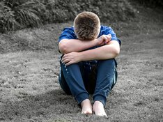 Das Foto zeigt einen Jungen, der traurig seinen Kopf in Arme und Schoß vergräbt.