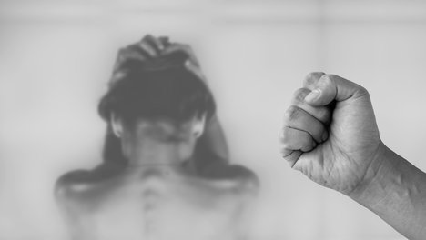Das Foto zur Pressemitteilung der Linken NRW zu "Corona-Pandemie: Mehr häusliche Gewalt gegen Frauen und Kinder befürchtet" zeigt im Vordergrund eine zur Faust geballte Hand und im Hintergrund einen Frauenoberkörper von hinten. 