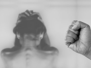 Das Foto zur Pressemitteilung der Linken NRW zu "Corona-Pandemie: Mehr häusliche Gewalt gegen Frauen und Kinder befürchtet" zeigt im Vordergrund eine zur Faust geballte Hand und im Hintergrund einen Frauenoberkörper von hinten. 
