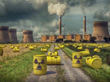 Das Foto zeigt gelbe Fässer mit einem Symbol für Radioaktivität darauf, die vor einem Atomkraftwerk liegen. 
