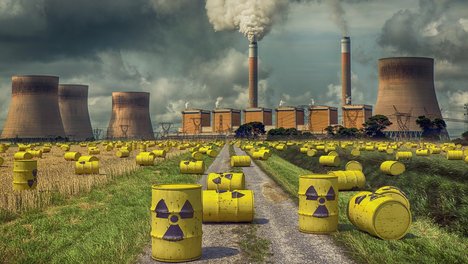 Das Foto zeigt gelbe Fässer mit einem Symbol für Radioaktivität darauf, die vor einem Atomkraftwerk liegen. 