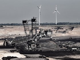 Das Foto zeigt den Tagebau Garzweiler, im Vordergrund Kohlebaggger, im Hintergrund Windräder.