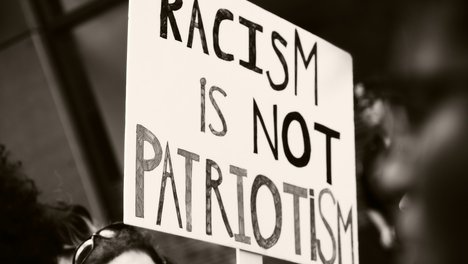 Das Foto zeigt ein Demo-Schils, auf dem "Racism is not Patriotism" steht. 