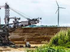LINKE NRW zu Hambi bleibt und RWE-Gewinn Das Foto zeigt einen Braunkohlebagger in einem Abbaugebiet sowie ein Stück Grünfläche und ein Windrad im Hintergrund