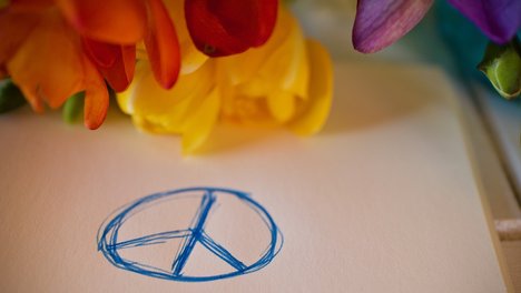 Das Foto zeigt ein Blatt Papier, auf dem das Friedenssymbol gezeichnet ist. 