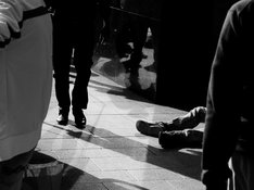 Das Foto in Schwarz-Weiß zeigt Menschen, die an einer obdachlosen Person vorbeigehen. 