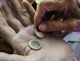 Das Bild zeigt die Hände einer alten Person, die zwei Euro halten. 