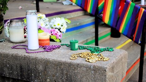 Das Foto zeigt im Hintergrund eine Girlande mit Regenbogenfahnen und im Vordergrund Kerzen, die auf der Mauer einer Treppe stehen. 