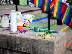 Das Foto zeigt im Hintergrund eine Girlande mit Regenbogenfahnen und im Vordergrund Kerzen, die auf der Mauer einer Treppe stehen. 