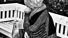 Das Foto zeigt eine Frau von hinten, die unter anderem ein Kopftuch trägt.