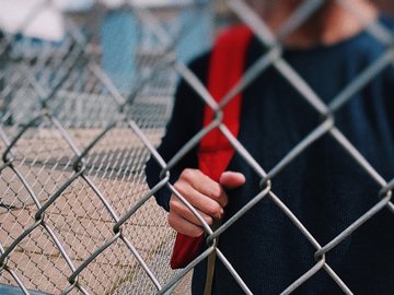 Das Foto zeigt einen Schüler, der hinter einem Zaun steht. 