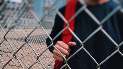 Das Foto zeigt einen Schüler, der hinter einem Zaun steht. 