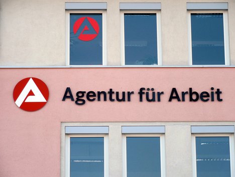 Das Foto zeigt eine Hausfassade, darauf ein Schild, auf dem "Agentur für Arbeit" steht.