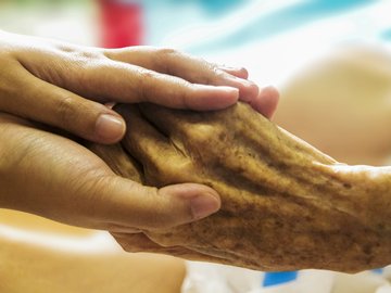 Das Foto zur Pressemitteilung der Linken NRW zum Tag der Pflege zeigt die Hände einer Pflegekraft, die die eines alten Menschen halten.