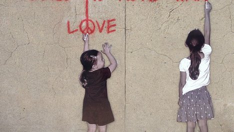 Das Foto zum Aufruf der Linken NRW zur Teilnahme an virtuellen Ostermärschen 2020 zeigt zwei Mädchen, die Make Love not War auf eine Hauswand schreiben.