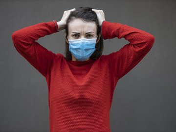 Das Foto zur Erklärung "Shopping King Laschet riskriert zweite Infektionswelle" zeigt eine Frau mit verzweifelter Geste, die einen Mund-Nasen-Schutz trägt. 