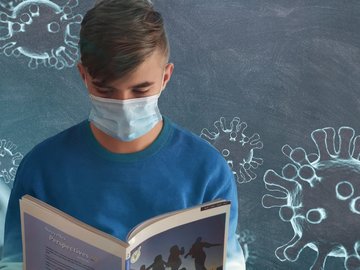 Das Foto zeigt einen Schüler, der in ein Schulbuch schaut. Er steht vor einer Tafel, auf die mit Kreise mit Viren gezeichnet sind.
