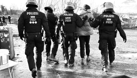 Das Foto zeigt Polizist:innen, die einen Aktivist abführen.