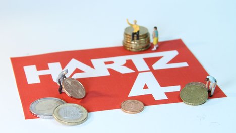 Das Foto zur Pressemitteilung der Linken NRW zu Laumanns Hartz IV-Sanktionen zeigt den Schriftzug Hartz IV. Darauf mühen sich kleine Figuren mit Kleingeld ab.